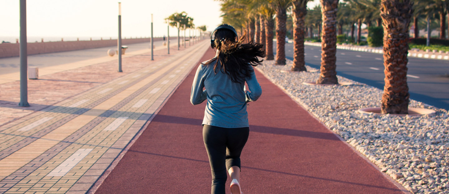 Woman running on a dedicated jogging track lined with palm trees along Abu Dhabi Corniche
