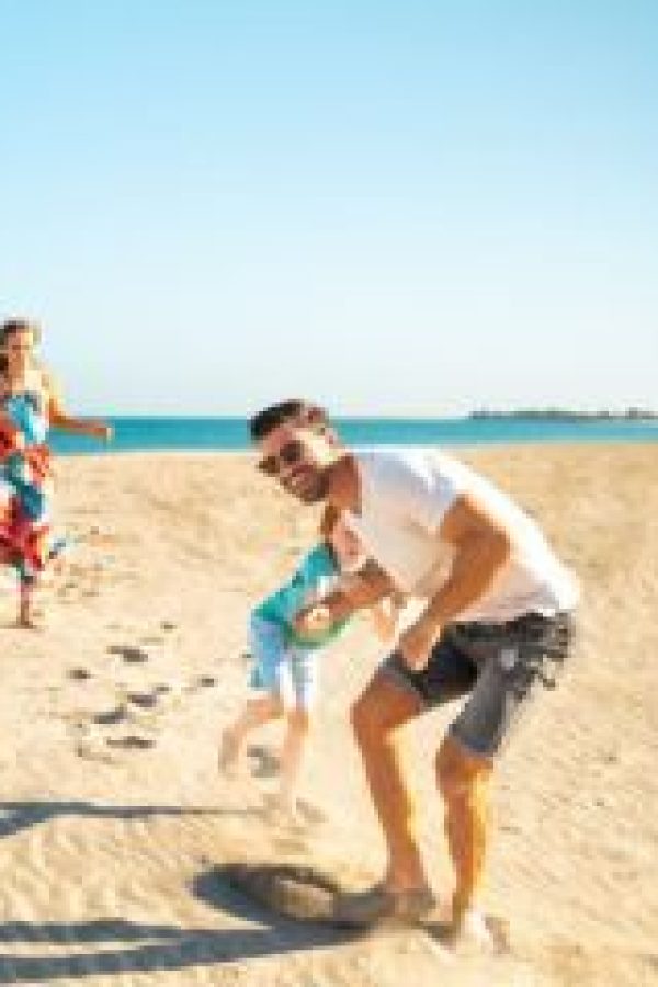 Happy family playing together on a sandy beach in Ras Al Khaimah with the sea in the background