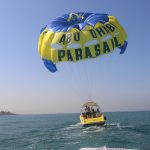 Abu Dhabi Parasail People enjoying a parasailing adventure over the turquoise waters of Abu Dhabi with a yellow and blue parachute labeled "Abu Dhabi Parasail".